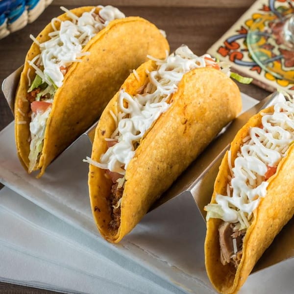 Three crispy tacos filled with meat, lettuce, tomatoes, and drizzled with sour cream.
