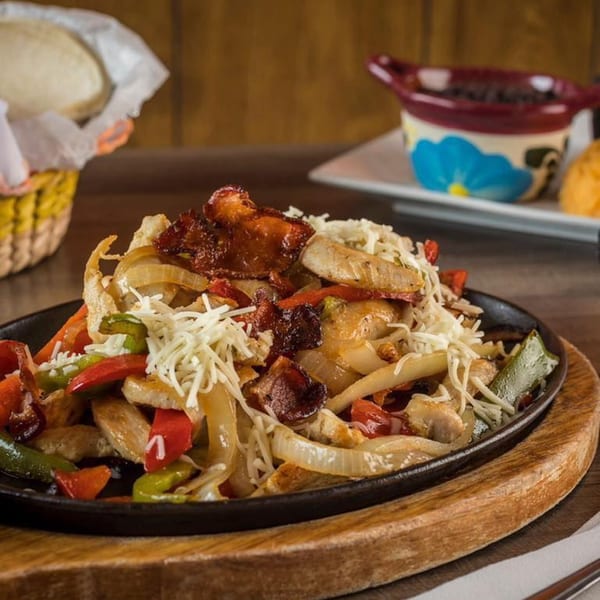 Sizzling chicken fajitas with bell peppers, onions, bacon, and shredded cheese on a cast iron platter.