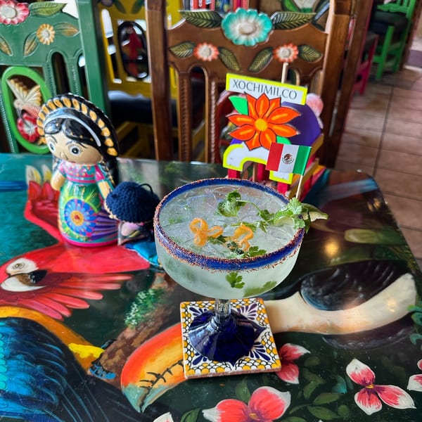A vibrant Mexican-themed table with a margarita, a doll, and a Xochimilco sign.