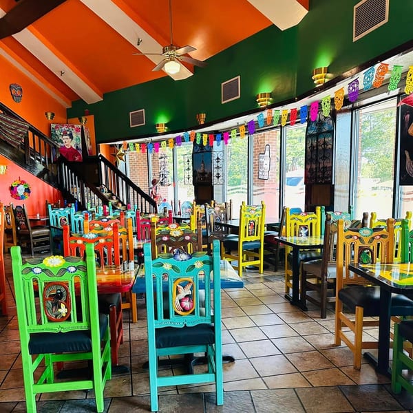 Vibrant Mexico City Taqueria interior with colorful chairs, tables, and festive decorations under orange and green walls.