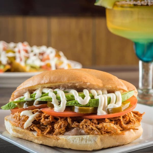 A Mexico City Taqueria torta with shredded chicken, avocado, tomato, and jalapeños, drizzled with crema.