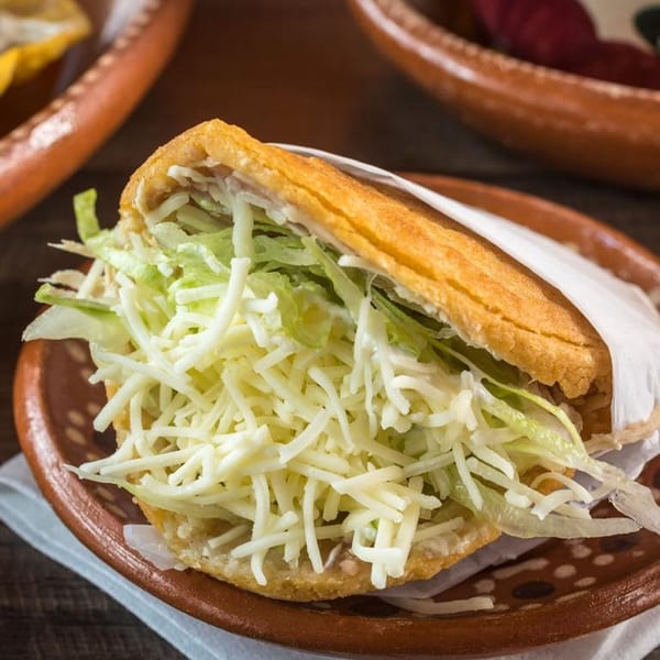 A Mexico City Taqueria gordita, filled with shredded lettuce and white cheese, on a brown plate.